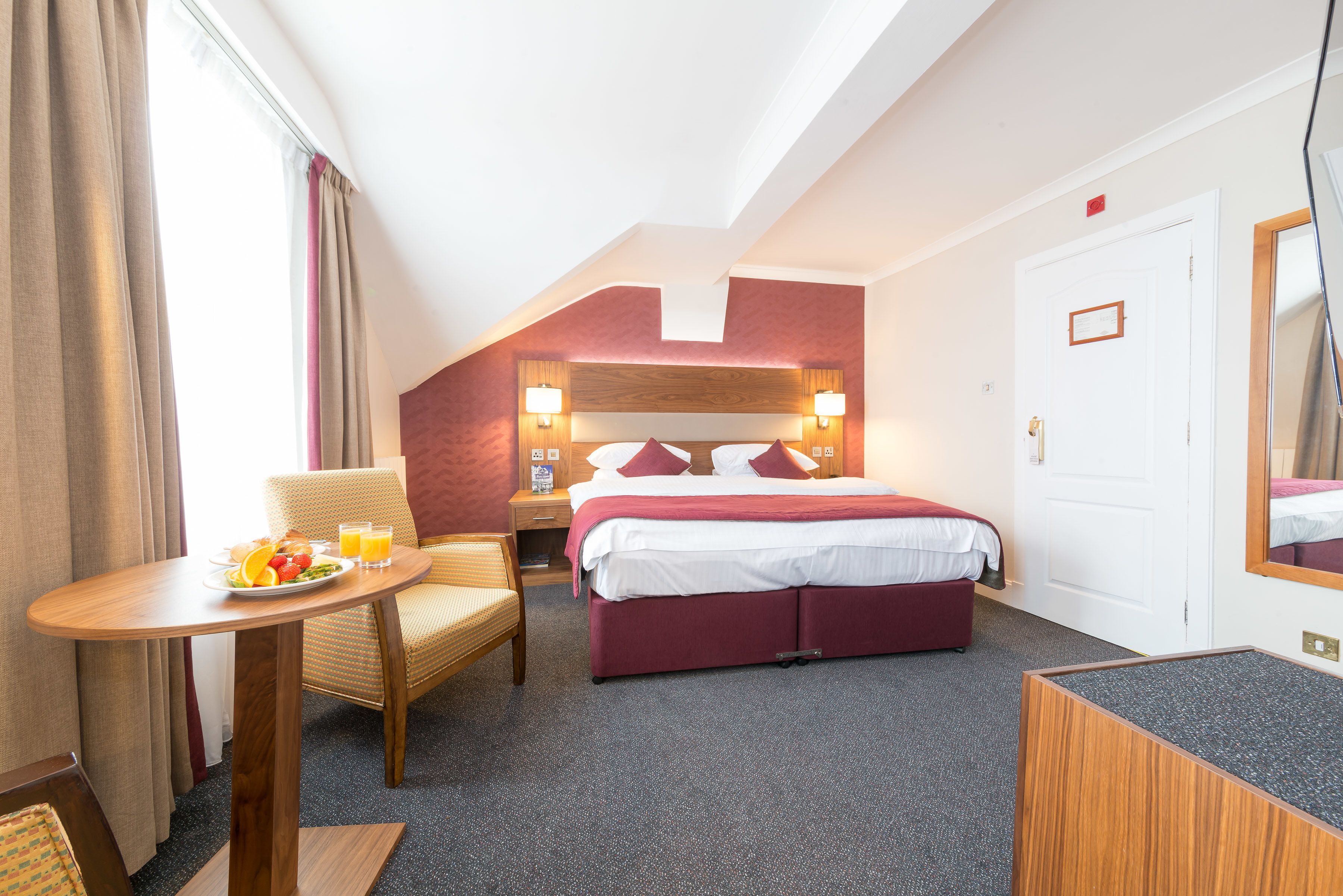A hotel room with a bed, a table with breakfast, a chair, and a desk.