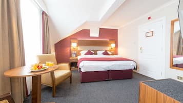 A hotel room with a bed, a table with breakfast, a chair, and a desk.