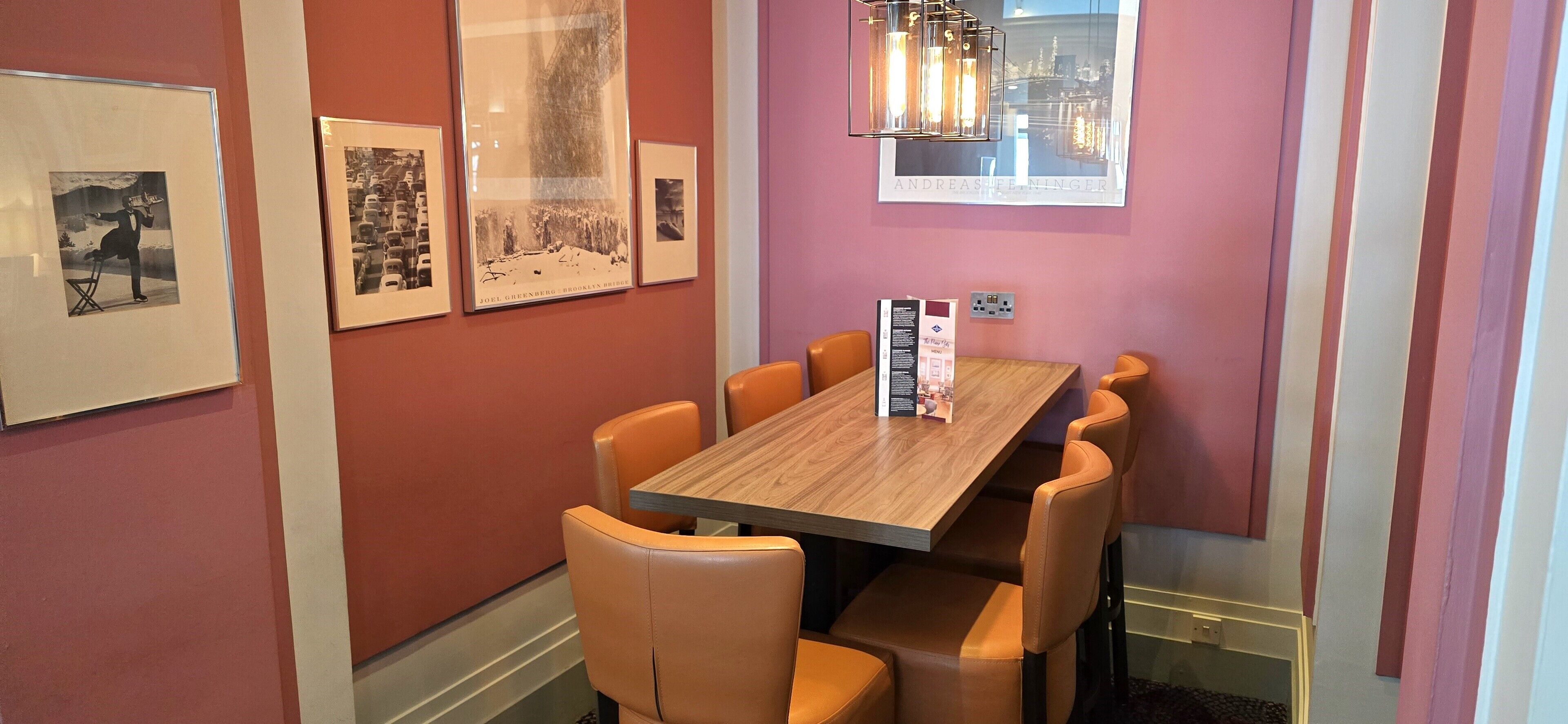 A dining area with a wooden table and six chairs, framed pictures on the wall, and a hanging light fixture.