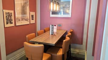 Un coin repas avec une table en bois et six chaises, des tableaux encadrés au mur et un luminaire suspendu.