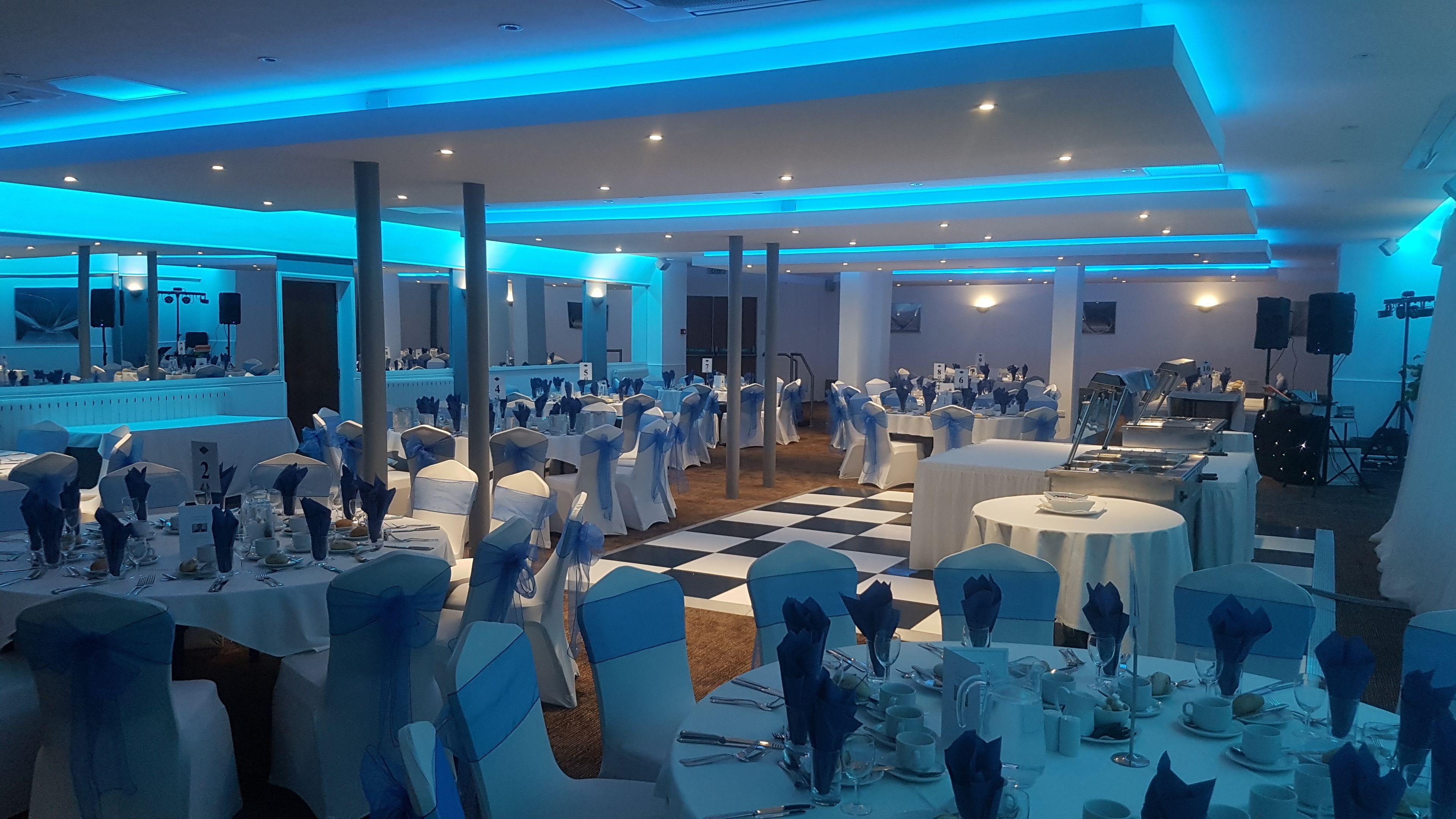 A banquet hall with tables set for a formal event, featuring white tablecloths and blue chair covers.