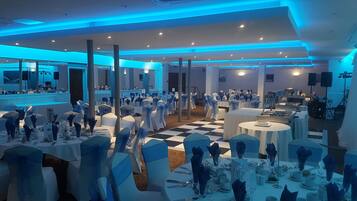 A banquet hall with tables set for a formal event, featuring white tablecloths and blue chair covers.