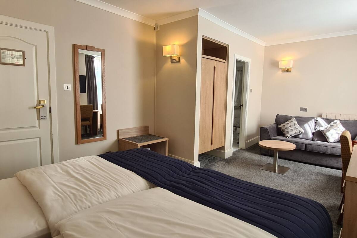 A hotel room with a bed, a sofa, a small table, a TV, and a wardrobe.