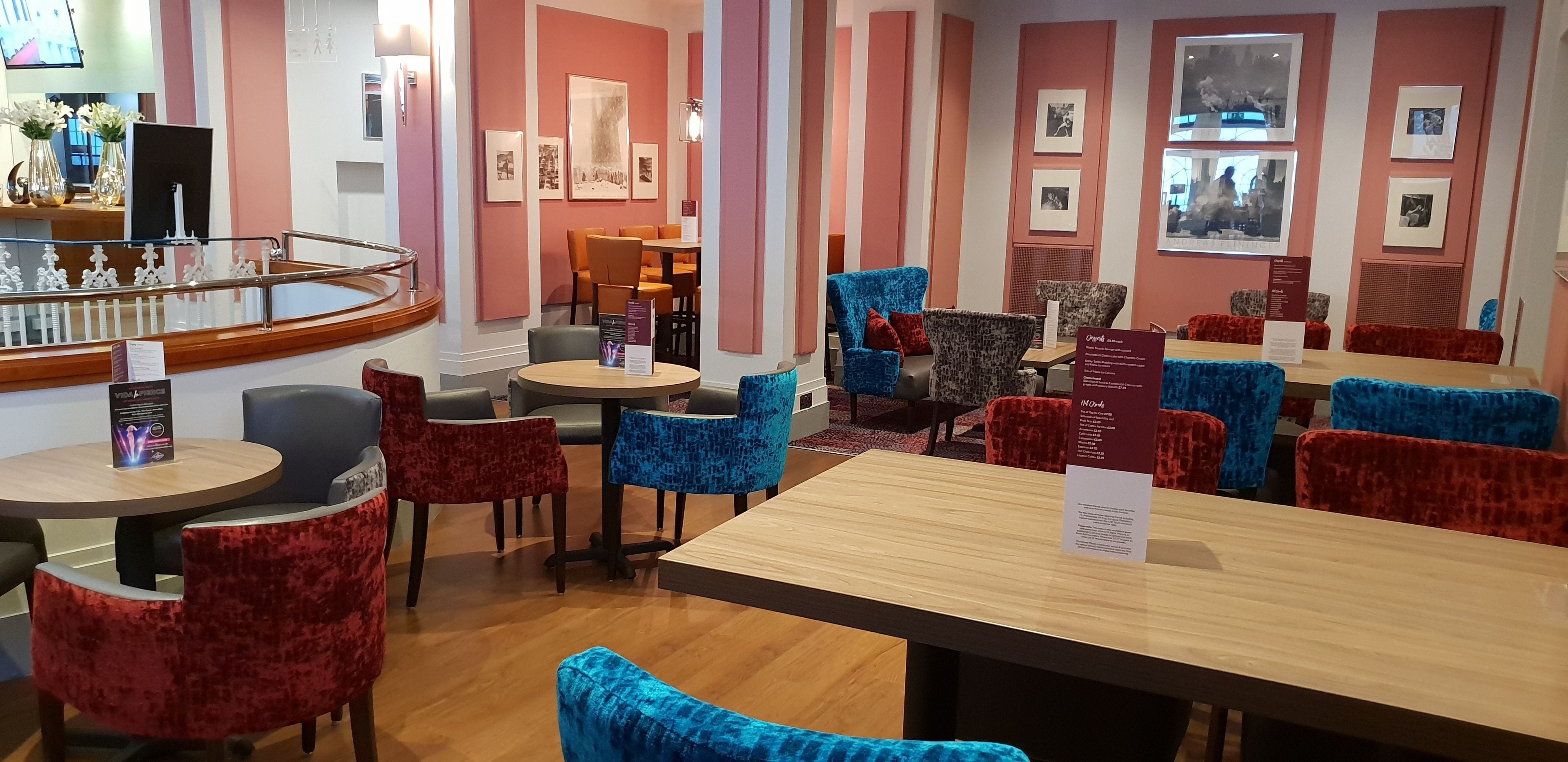 A hotel lobby with round tables and chairs, a bar area, and framed pictures on the walls.