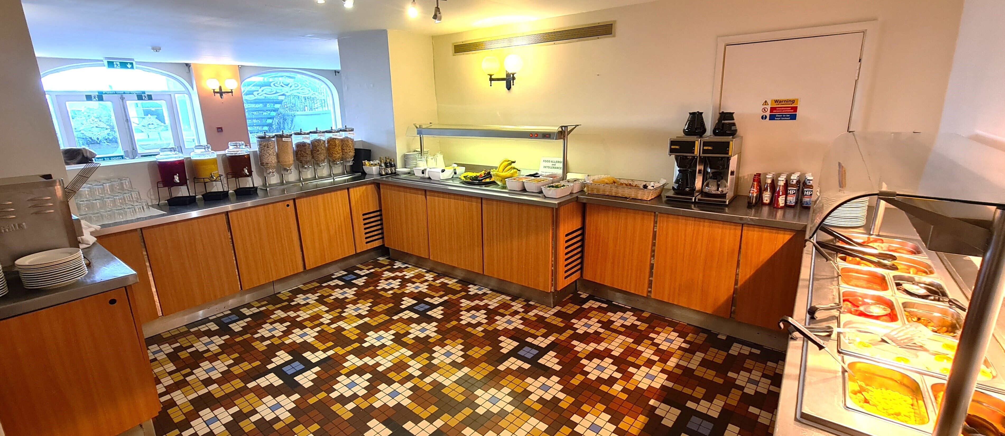 A kitchen area with a tiled floor, a food allergy warning sign, and a coffee machine.