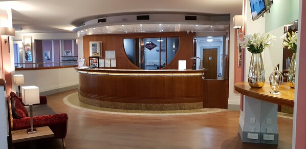 Experience the warm welcome at our lobby, featuring a curved reception desk and comfortable seating area.