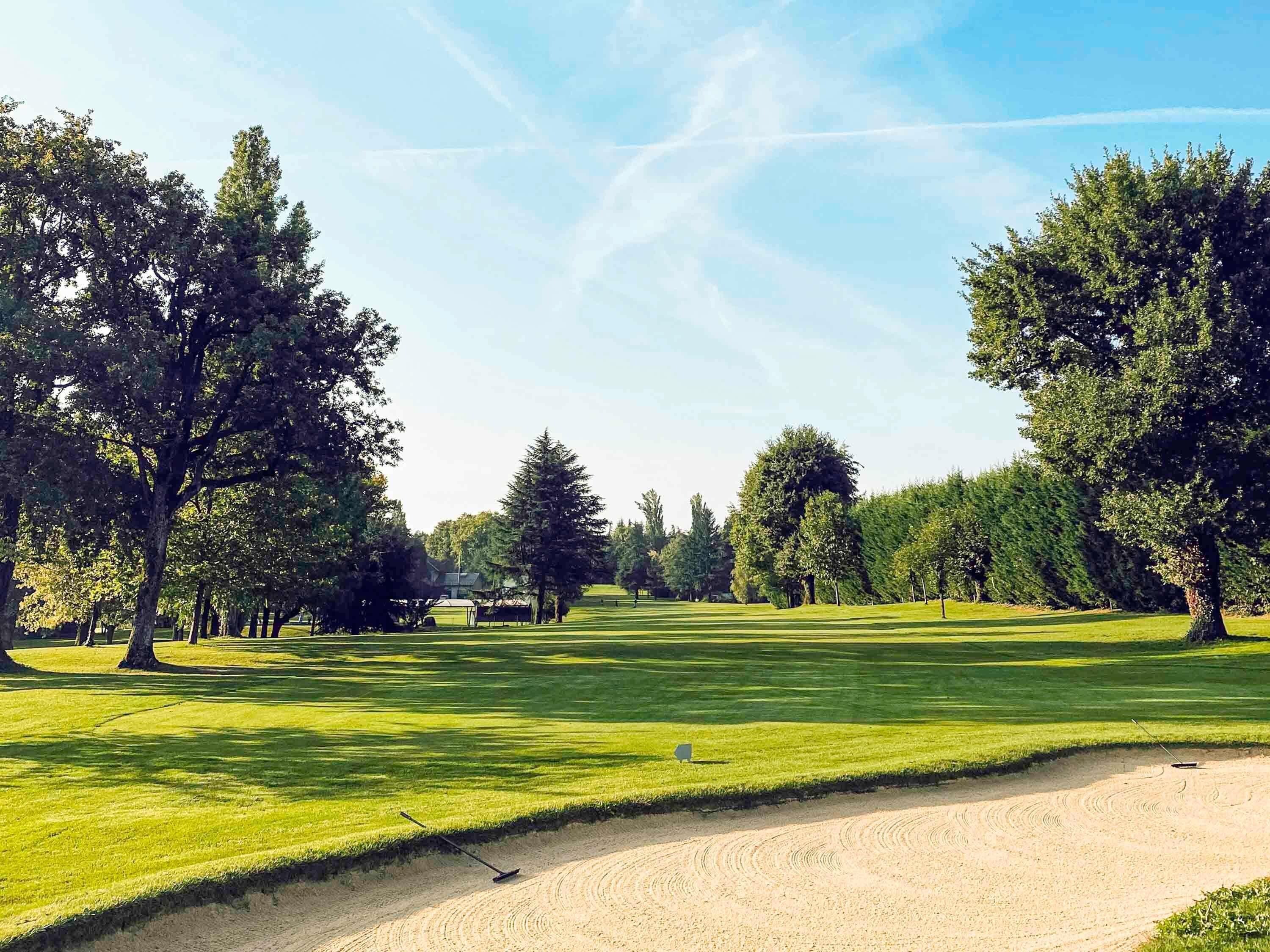 En golfbana med sandbunkrar, träd och en klar himmel.