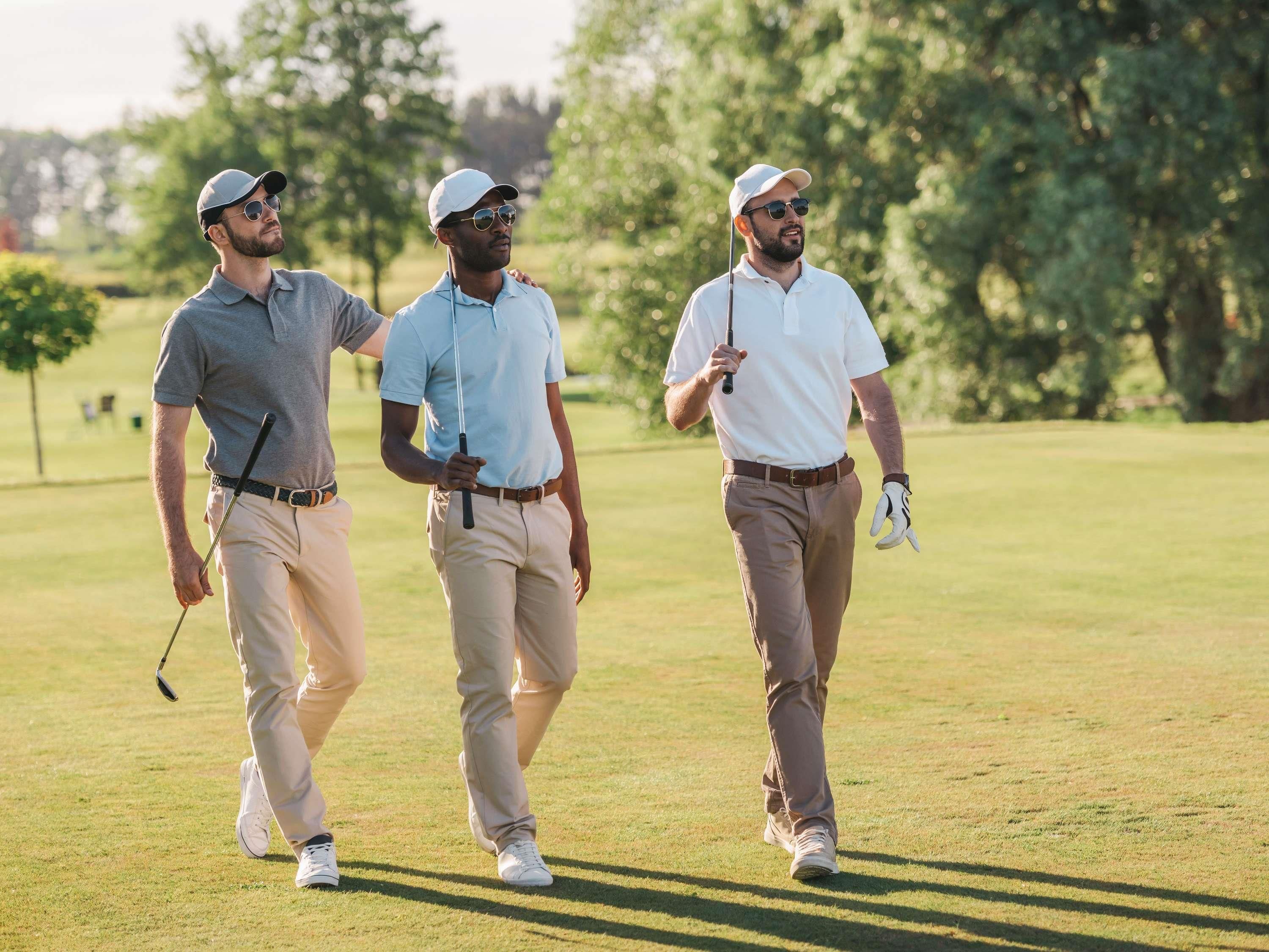 Three individuals walking on a golf course with trees in the background.