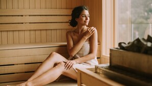 A person sitting on a wooden bench in a room with a large window, wooden walls, and a sauna. - Mercure Hotel & Spa Aix-les-Bains Domaine Marlioz (Aix-les-Bains)