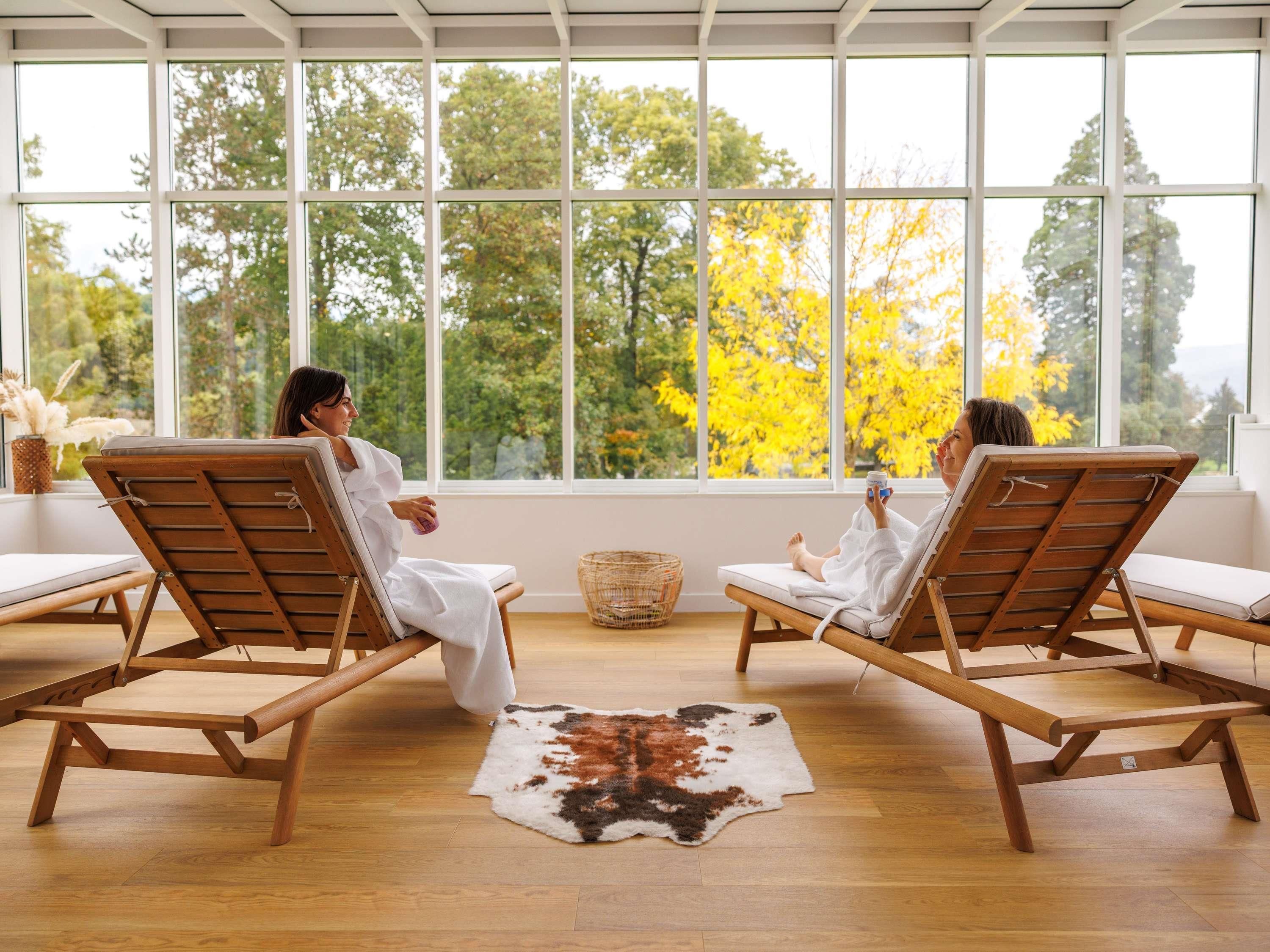 Two lounge chairs facing each other with a view of trees through large windows.