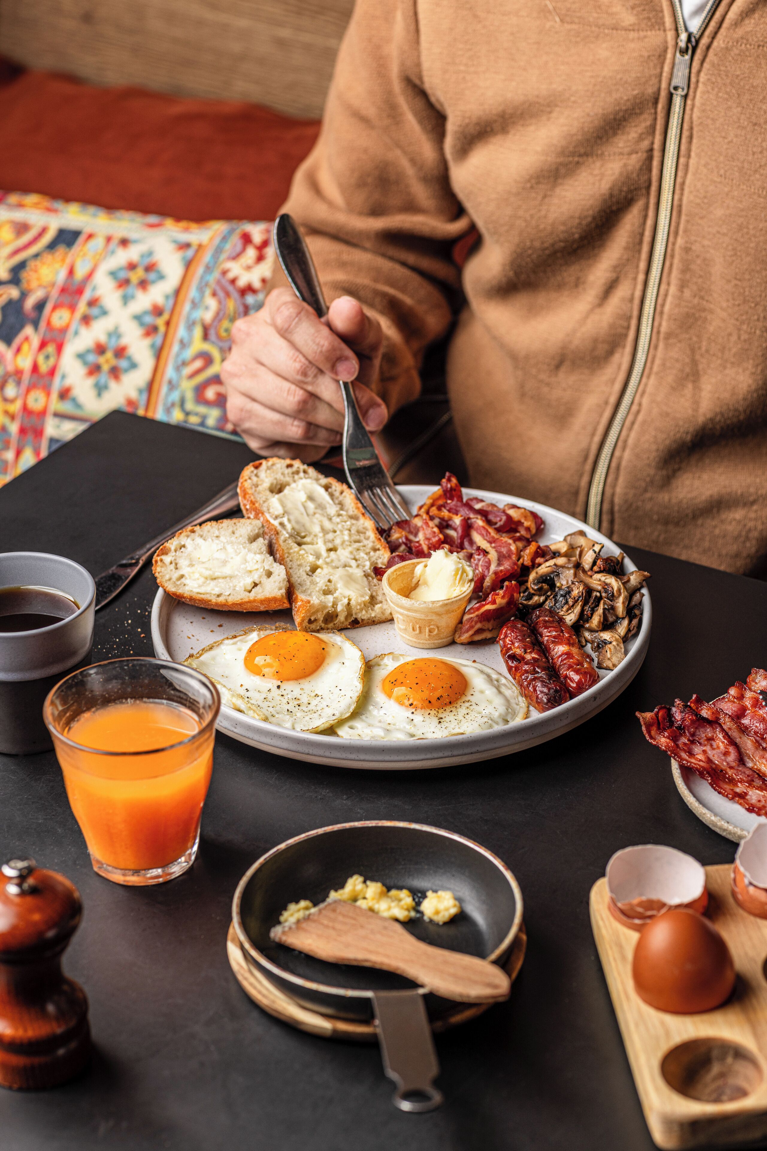A breakfast plate with eggs, bacon, sausages, and toast, accompanied by a glass of orange juice and a cup of coffee.