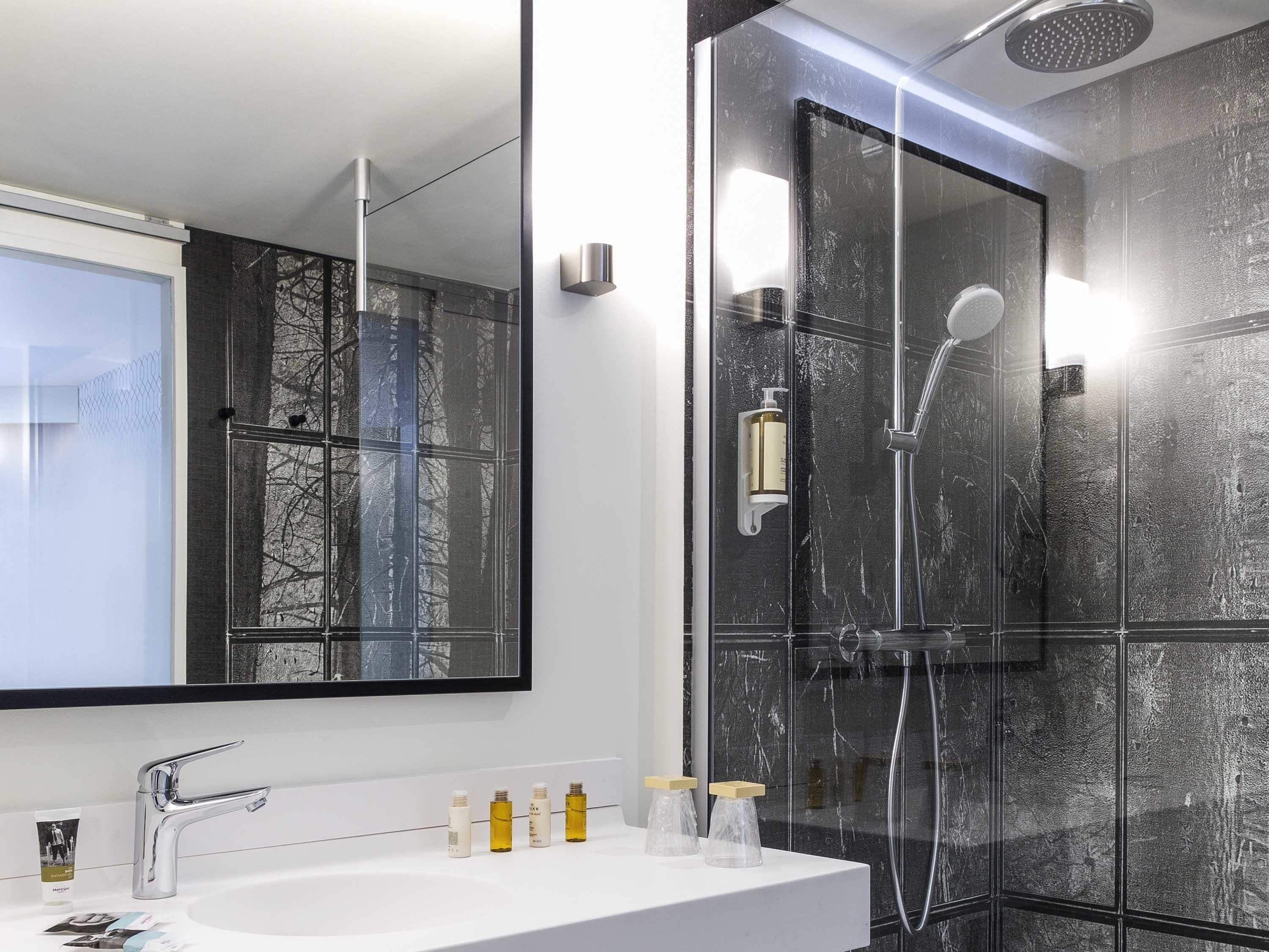Un bany modern amb un mirall gran, un espai de banyera i un lavabo blanc amb articles de tocador.