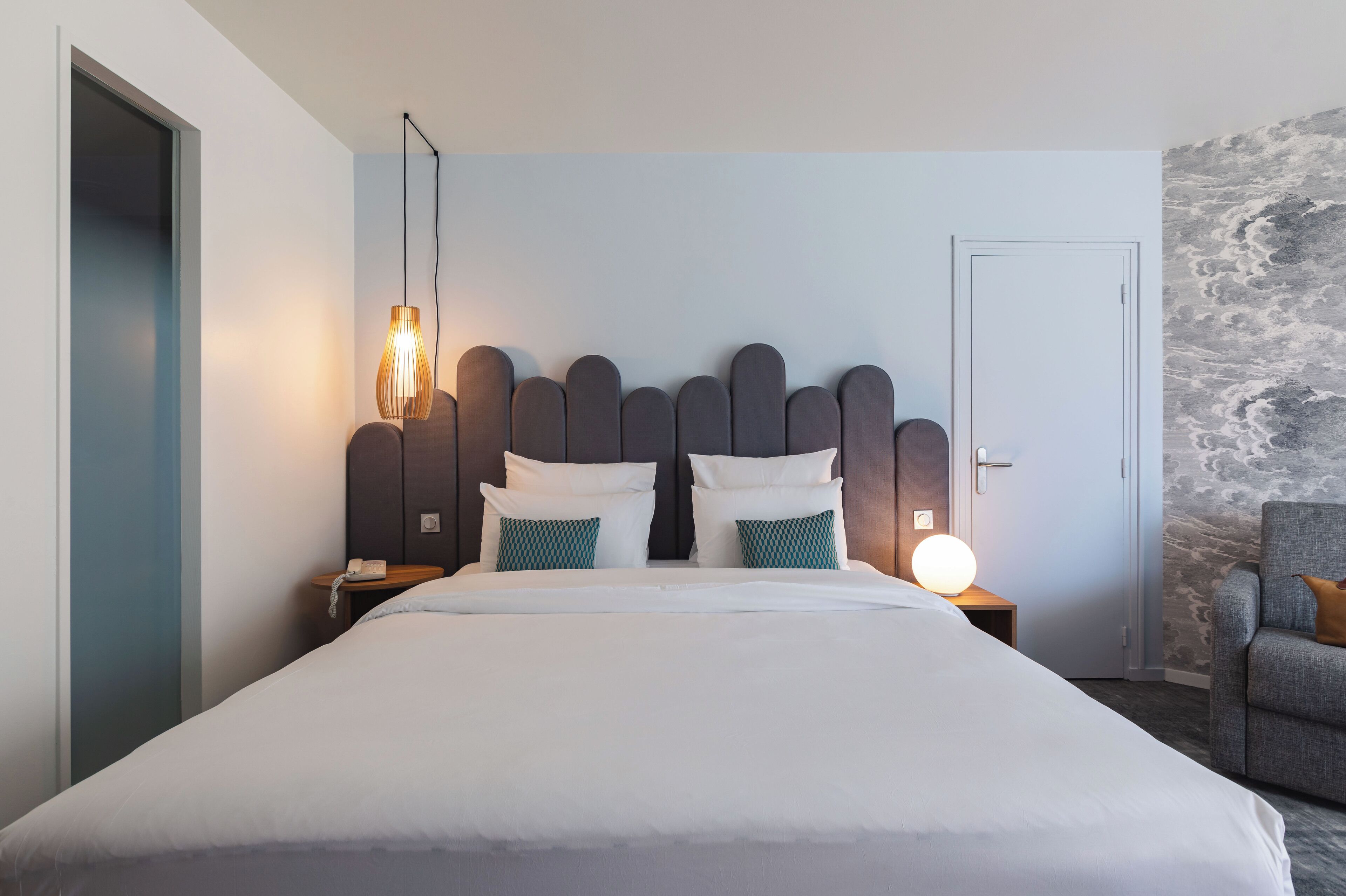 Et moderne hotelværelse med en stor seng, en sengegavl med unikt design, natlamper og en stol.