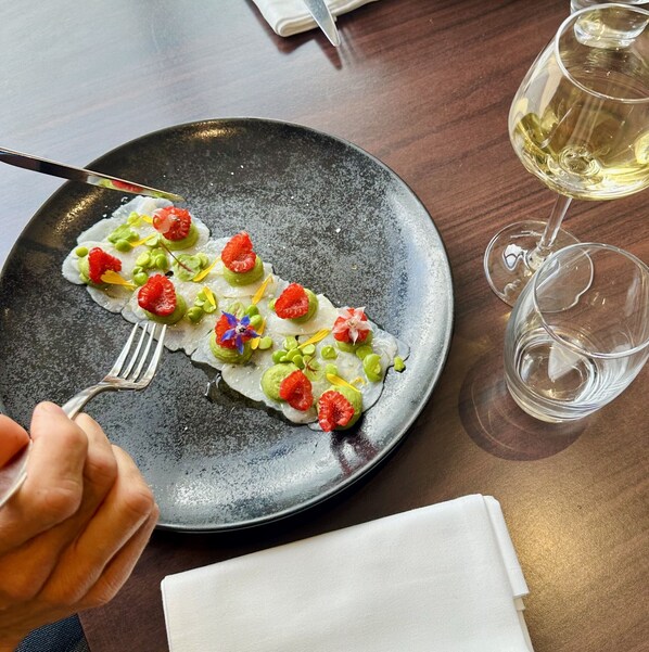 Un plato de comida con un tenedor, una servilleta y dos copas de vino blanco sobre una mesa.