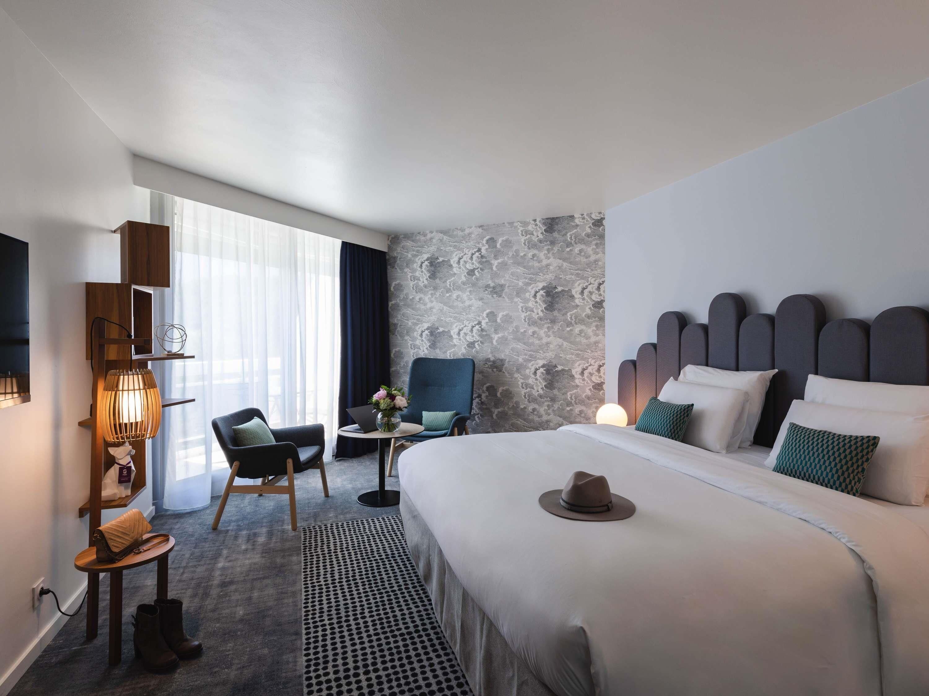 Ett hotellrum med en stor säng, ett skrivbord, en stol och en vägg av sten.
