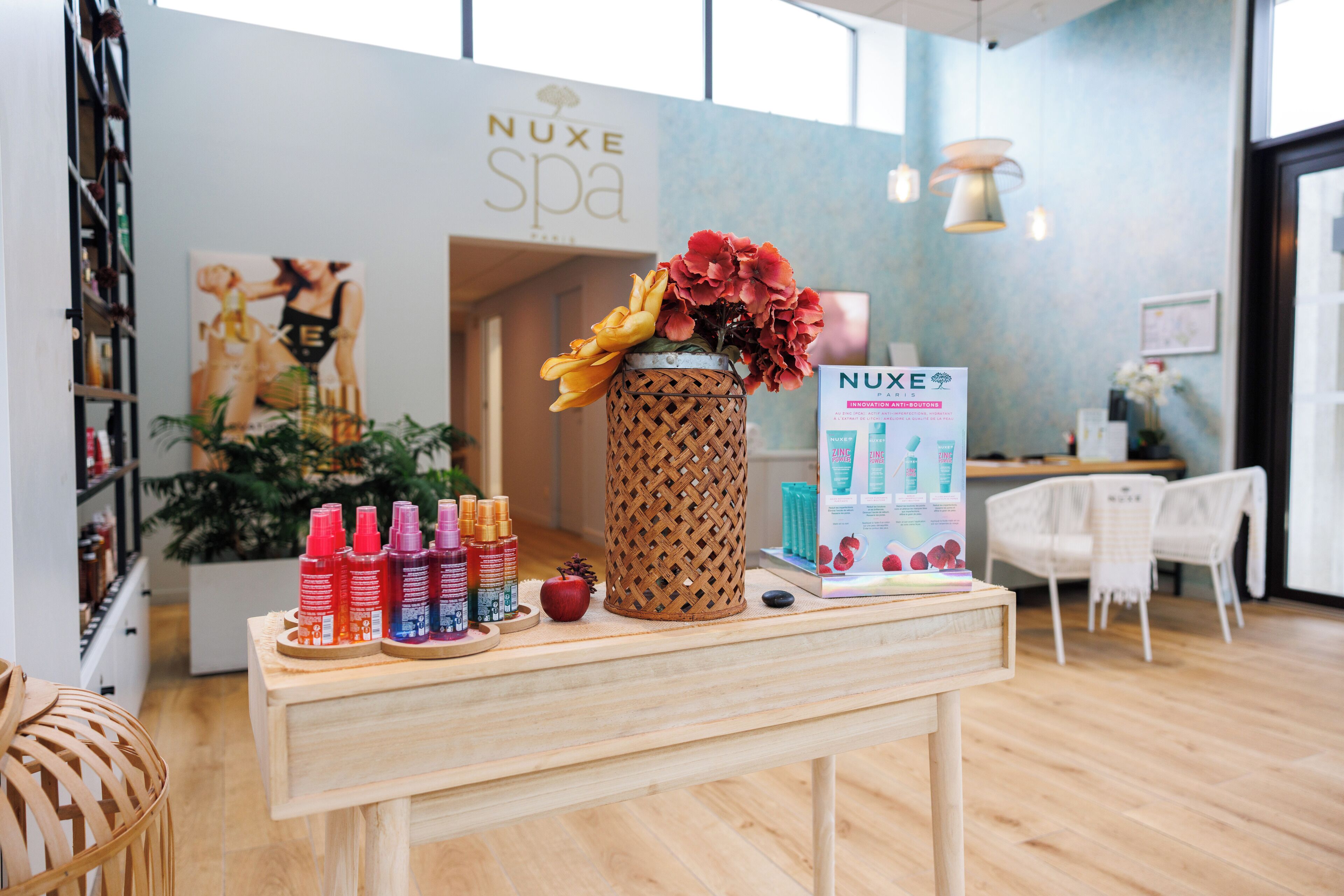 A spa area with a wooden table displaying various products, a decorative vase with flowers, and a sign for NUXE spa.