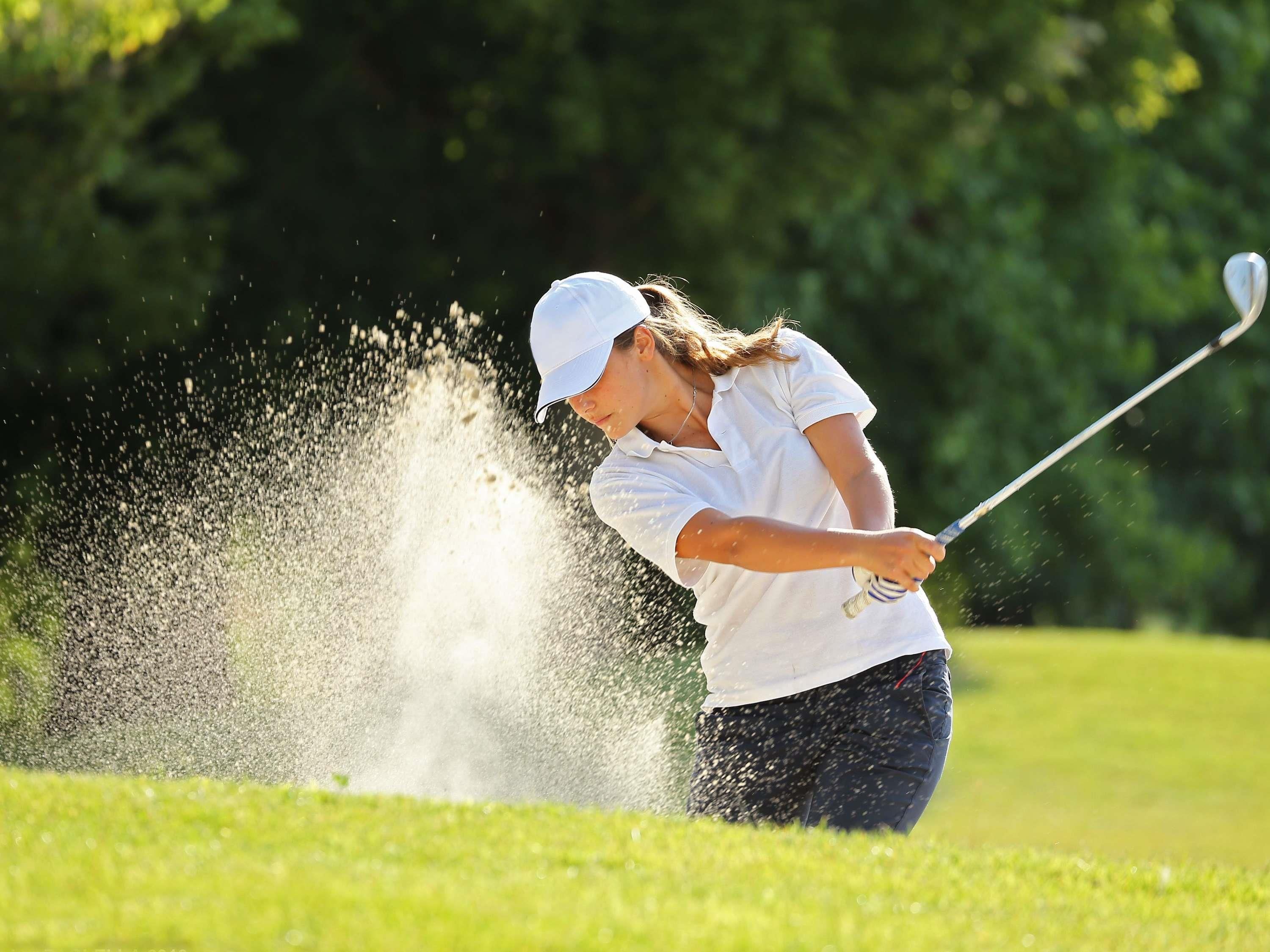 A person playing golf, hitting a ball that causes a dust cloud.