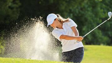A person playing golf, hitting a ball that causes a dust cloud.
