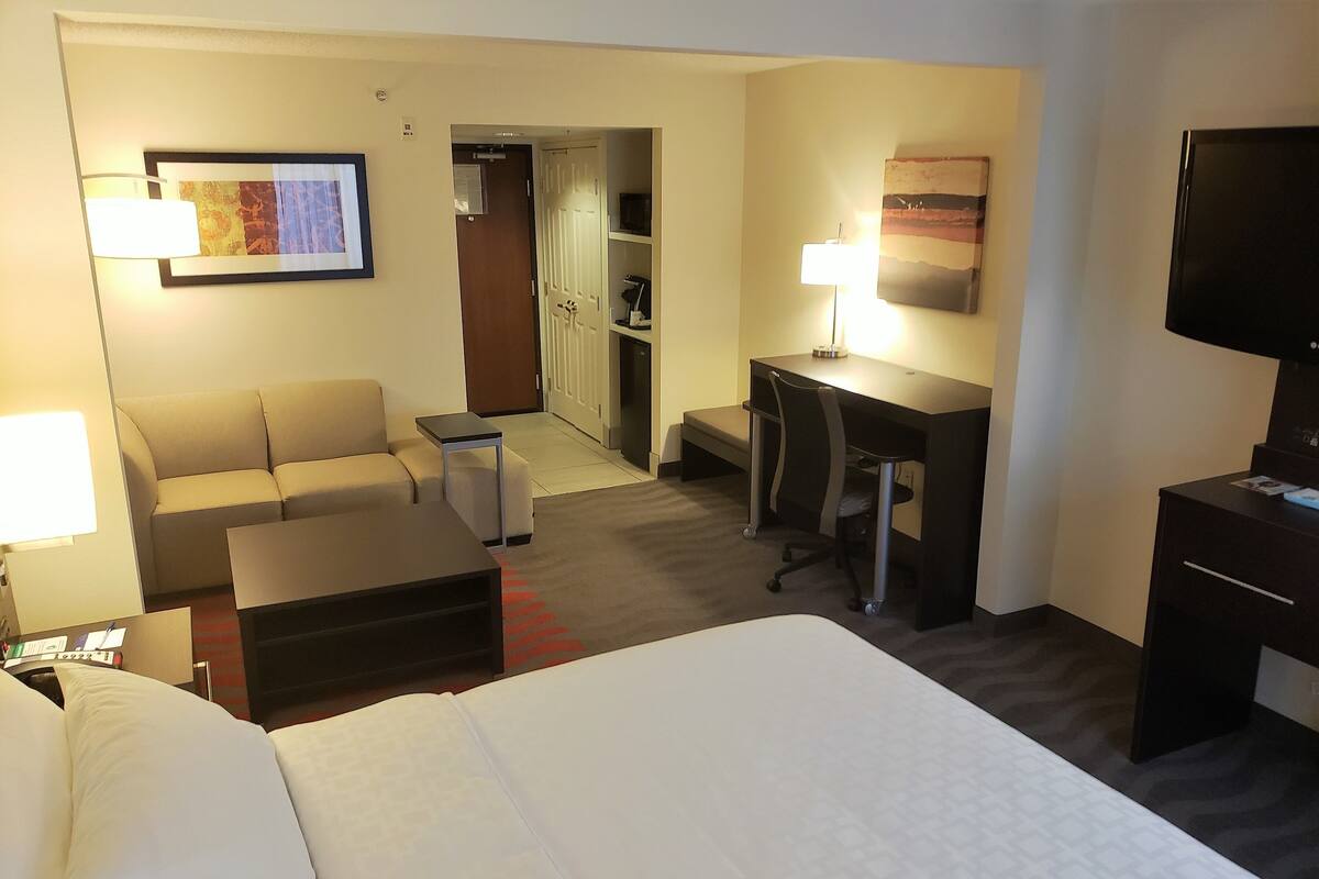 Una habitación de hotel con cama, escritorio, silla, sofá y televisor.