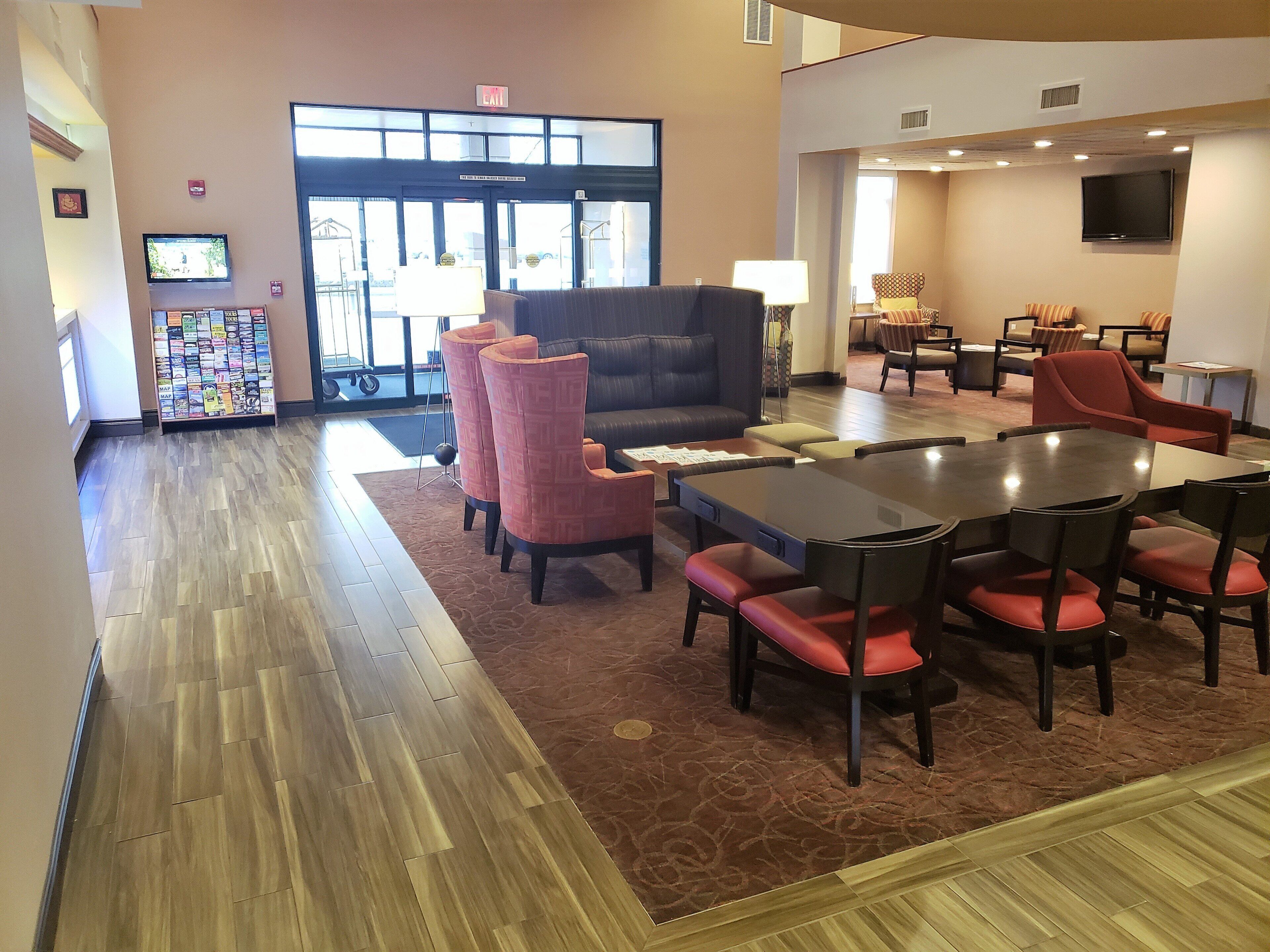 A hotel lobby with a large seating area, a reception desk, and a TV screen.