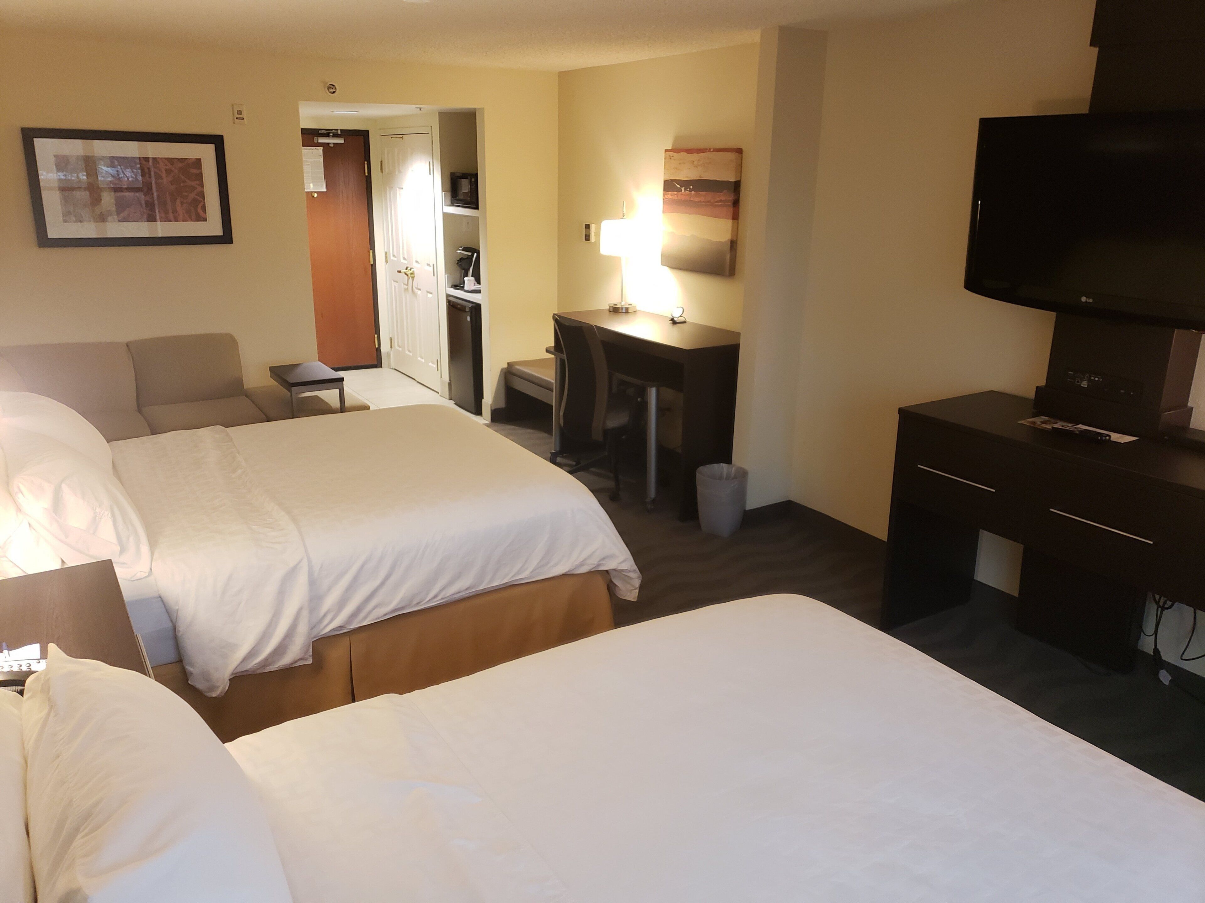 Een hotelkamer met twee bedden, een bureau, een stoel, een televisie en een deur naar een badkamer.