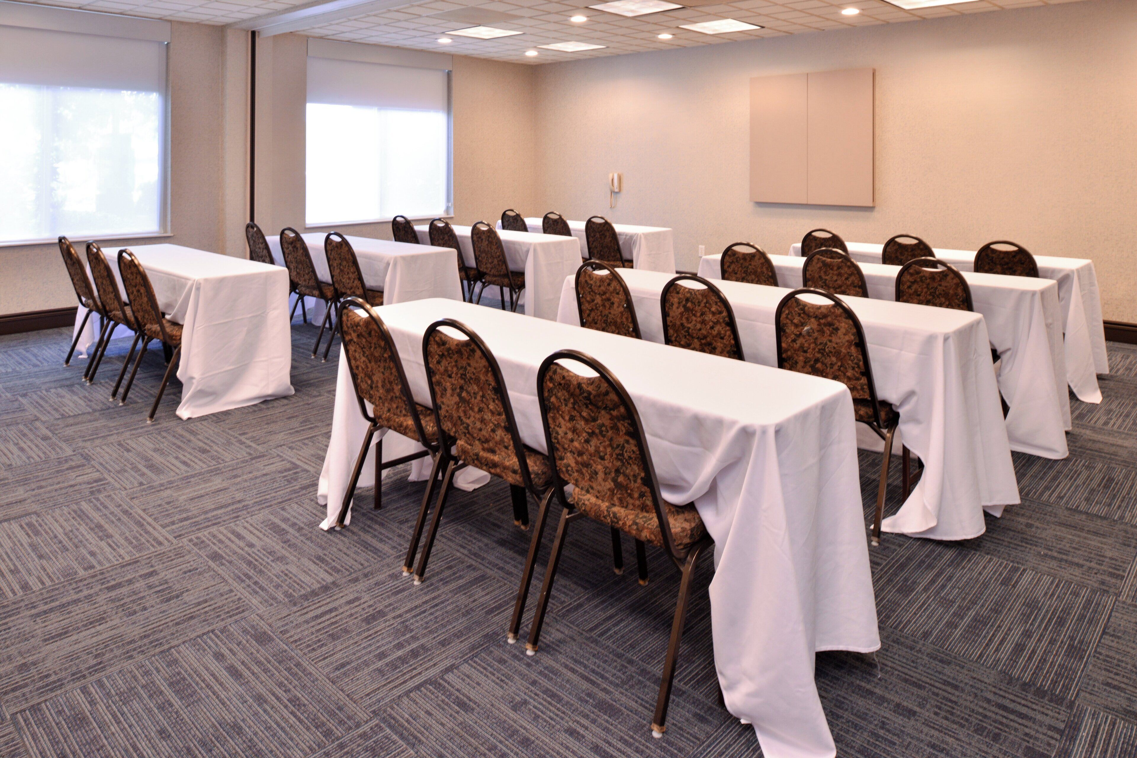A conference room with multiple tables and chairs, carpeted flooring, and a projector screen on the wall.
