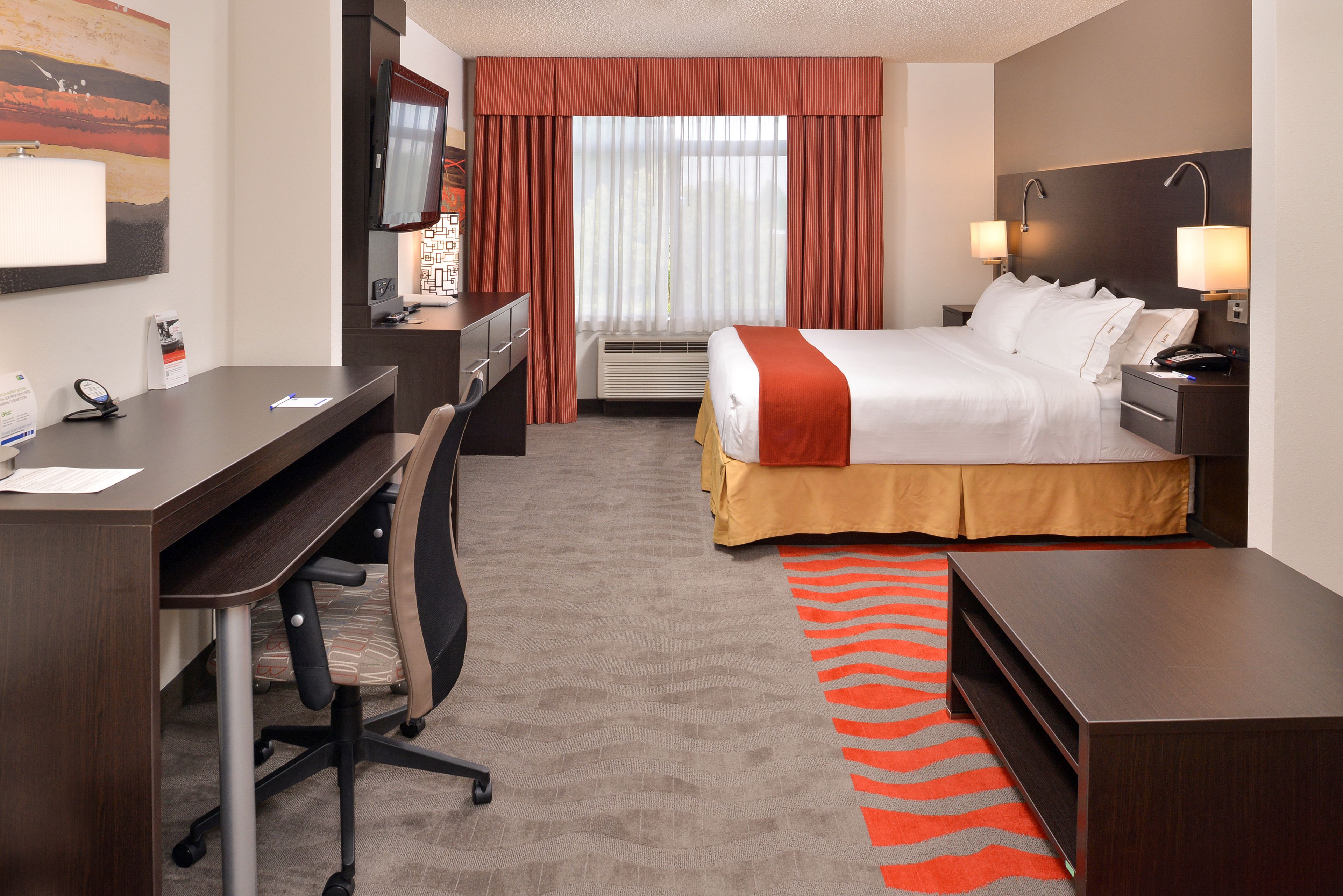 Une chambre d’hôtel avec un lit, un bureau, une chaise et une grande fenêtre avec des rideaux.