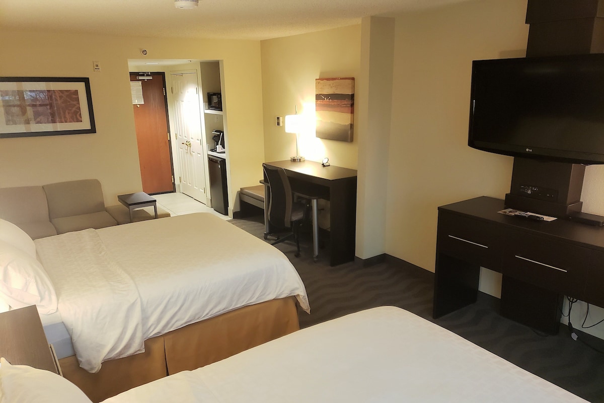 A hotel room with two beds, a desk, a chair, a television, and a desk lamp.