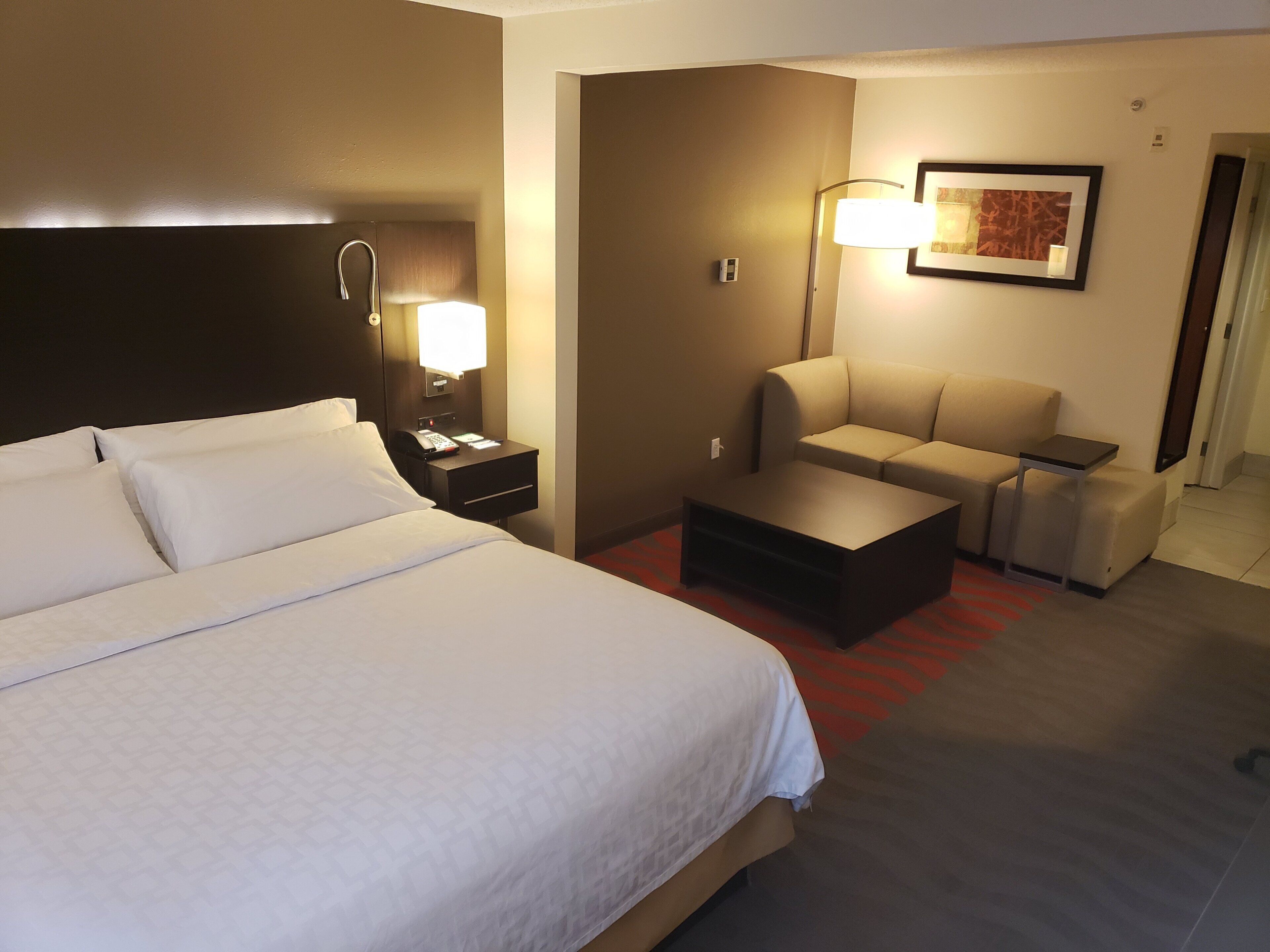 Ett hotellrum med en stor säng, ett skrivbord med en telefon, en soffa och en lampa.
