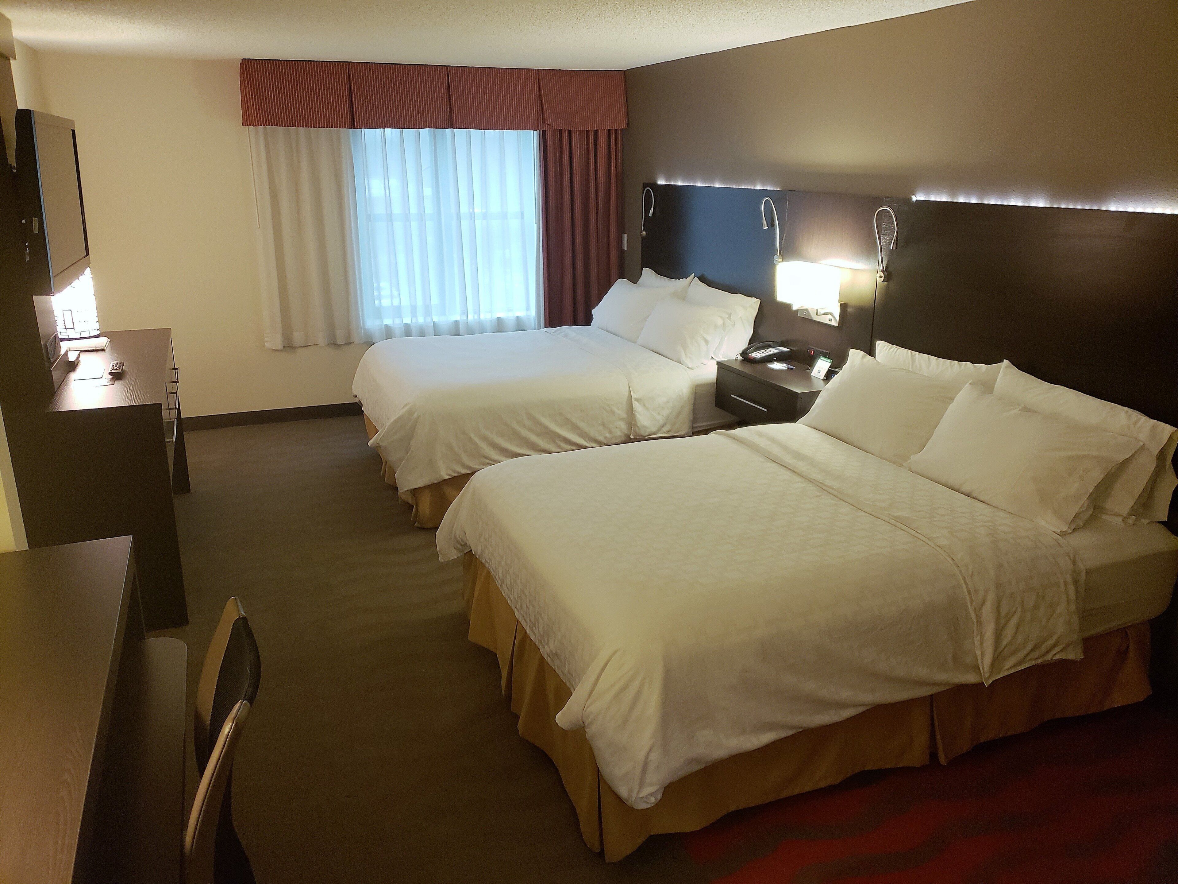 Une chambre d’hôtel avec deux lits, un bureau, une chaise, une table de chevet et une fenêtre avec des rideaux.