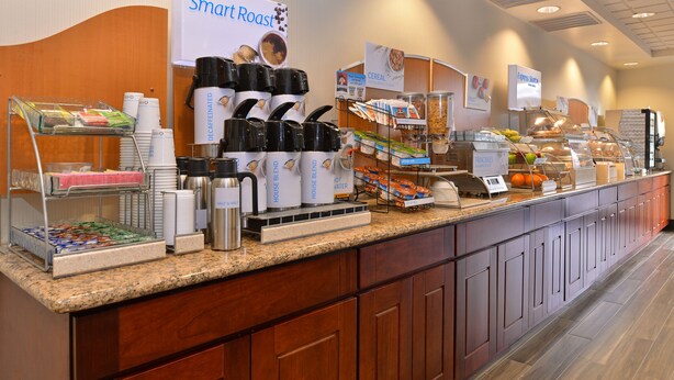 A buffet counter with coffee machines, cereal, and fruit options.