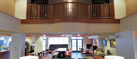A hotel lobby with a dining area, seating arrangements, and a staircase leading to an upper level.
