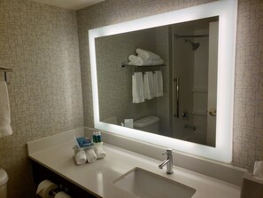 A bathroom with a large mirror, a sink, and a toilet. There are towels and toiletries on the sink. - Holiday Inn Express Portland West/Hillsboro by IHG (Hillsboro)