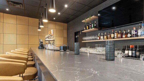 Un área de bar con una barra larga, asientos y estanterías llenas de botellas y vasos.
