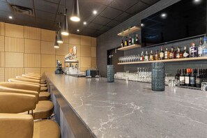 A bar area with a long counter, seating, and shelves of bottles and glasses. - Prestige Golden Hotel (Golden)