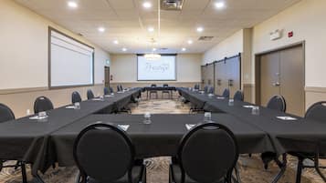 Ein Konferenzraum mit einem langen Tisch, Stühlen, einer Projektionsleinwand und einem Teppichboden.