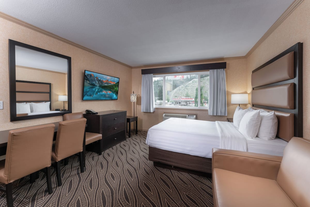A hotel room with a bed, a desk, a chair, a TV, and a window with a view of a mountain.