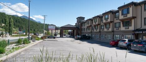 A hotel with multiple floors, a parking lot with several cars, and a mountainous backdrop.