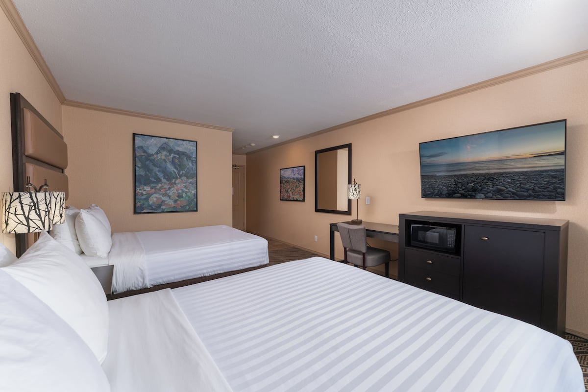 A hotel room with two beds, a desk, a chair, a television, and artwork on the walls.