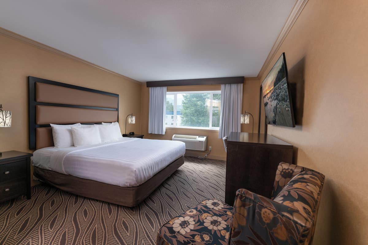 A hotel room with a large bed, a desk, a chair, a window with curtains, and a painting on the wall.