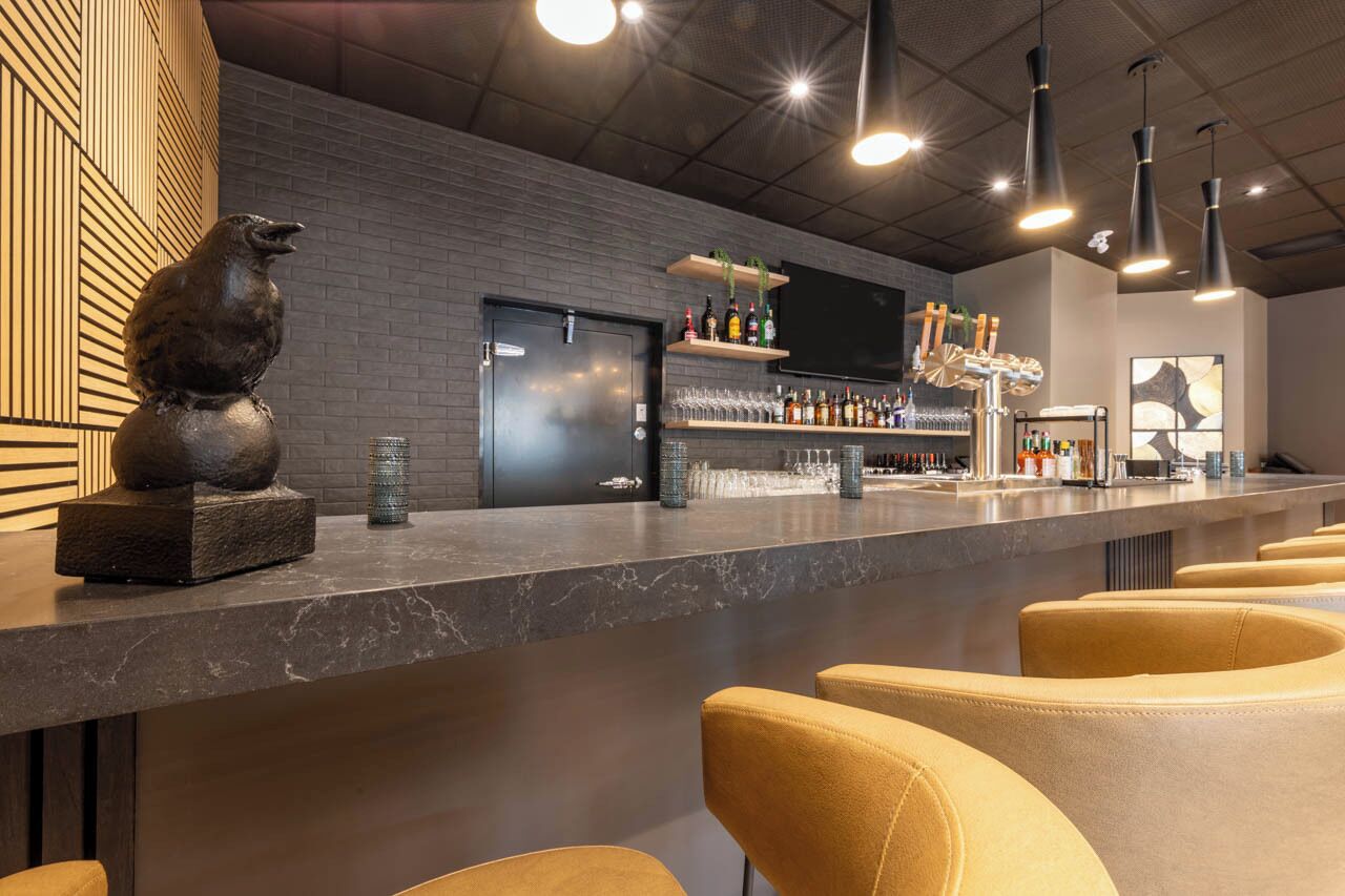 Een bar met een marmeren aanrecht, barkrukken, een aan de muur bevestigde televisie en planken met flessen en glazen.