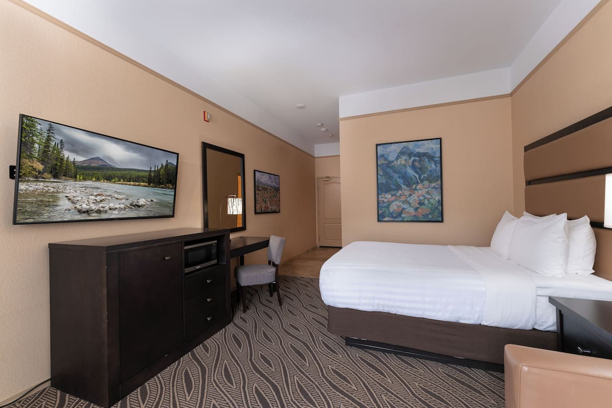 A hotel room with a large bed, a desk, a chair, and two paintings on the walls.