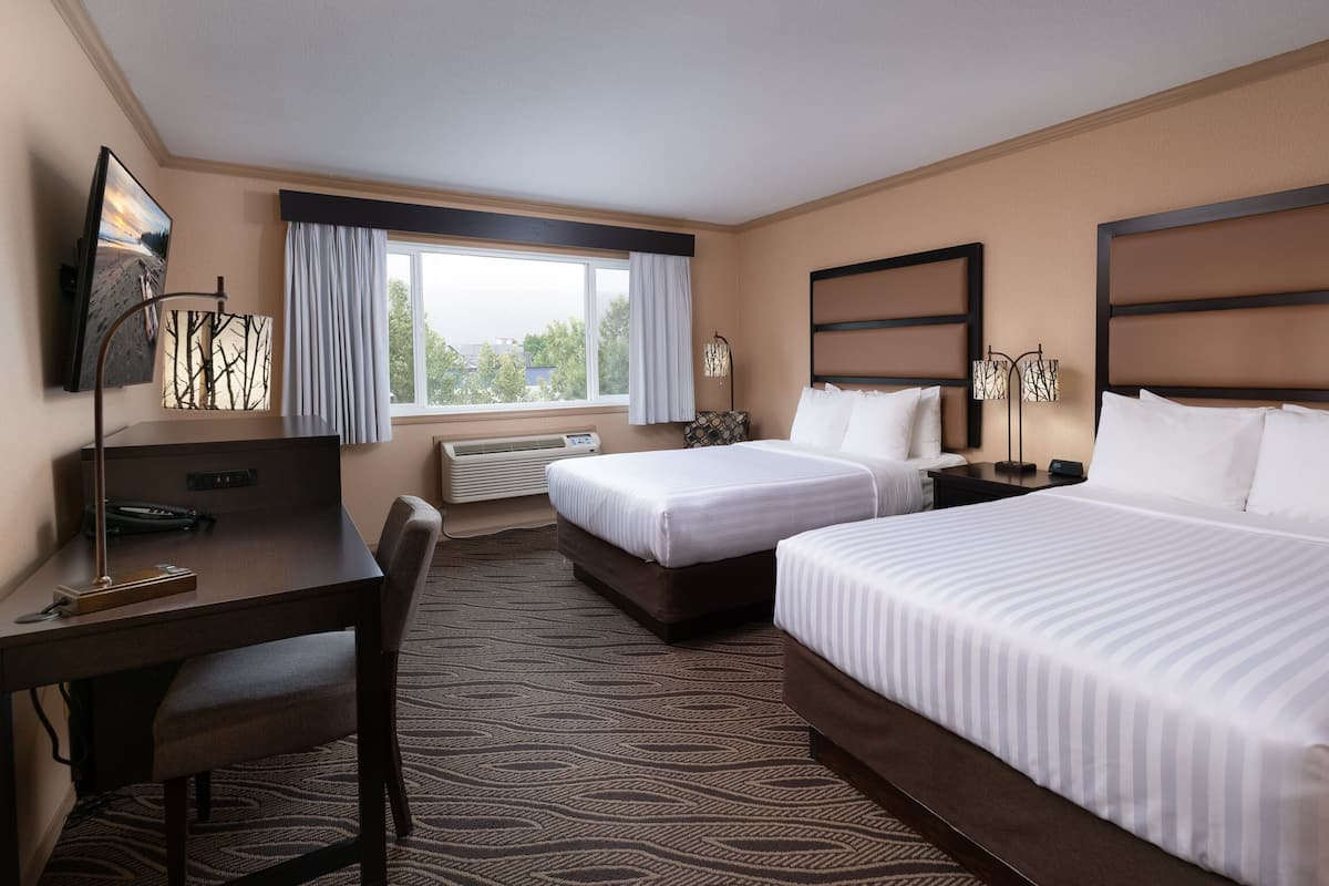 A hotel room with two beds, a desk, a chair, a lamp, and a window with curtains.
