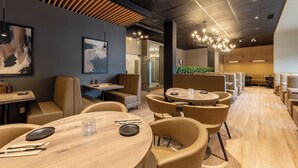 Un restaurante moderno con mesas redondas y cabinas, paneles de techo de madera e iluminación contemporánea.