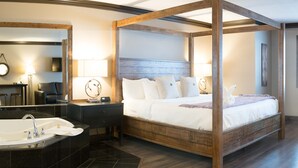 Una cama con dosel con sábanas blancas, un espejo grande, una bañera independiente y suelo de madera.