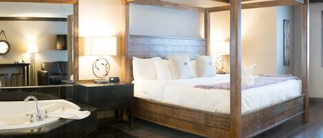 A four-poster bed with white linens, a large mirror, a standalone bathtub, and a wooden floor.