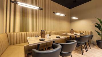 Un restaurant moderne avec des banquettes et des tables rectangulaires, agrémenté de lambris en bois sur les murs et d’un éclairage suspendu.