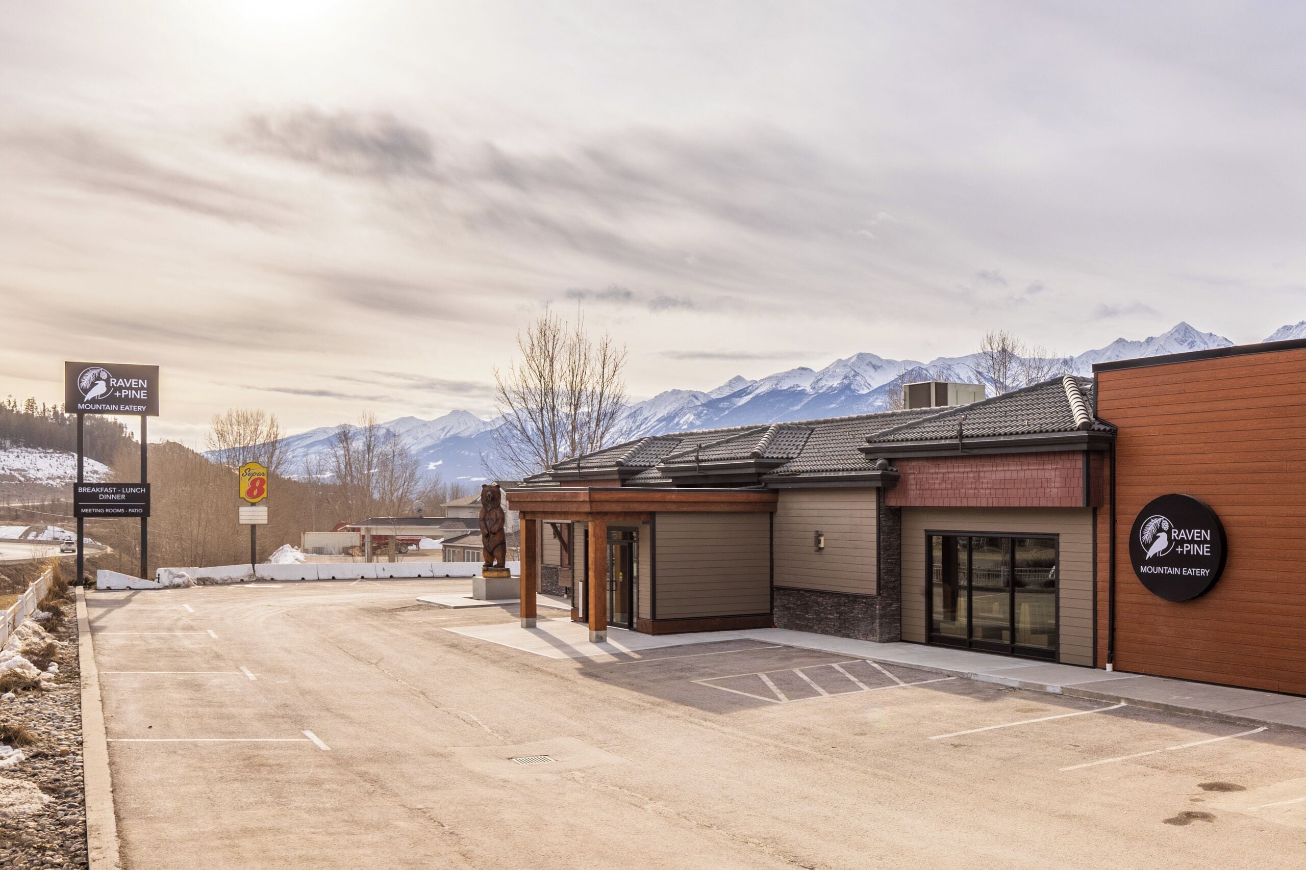 A mountain restaurant with a parking lot and a view of snow-capped mountains.