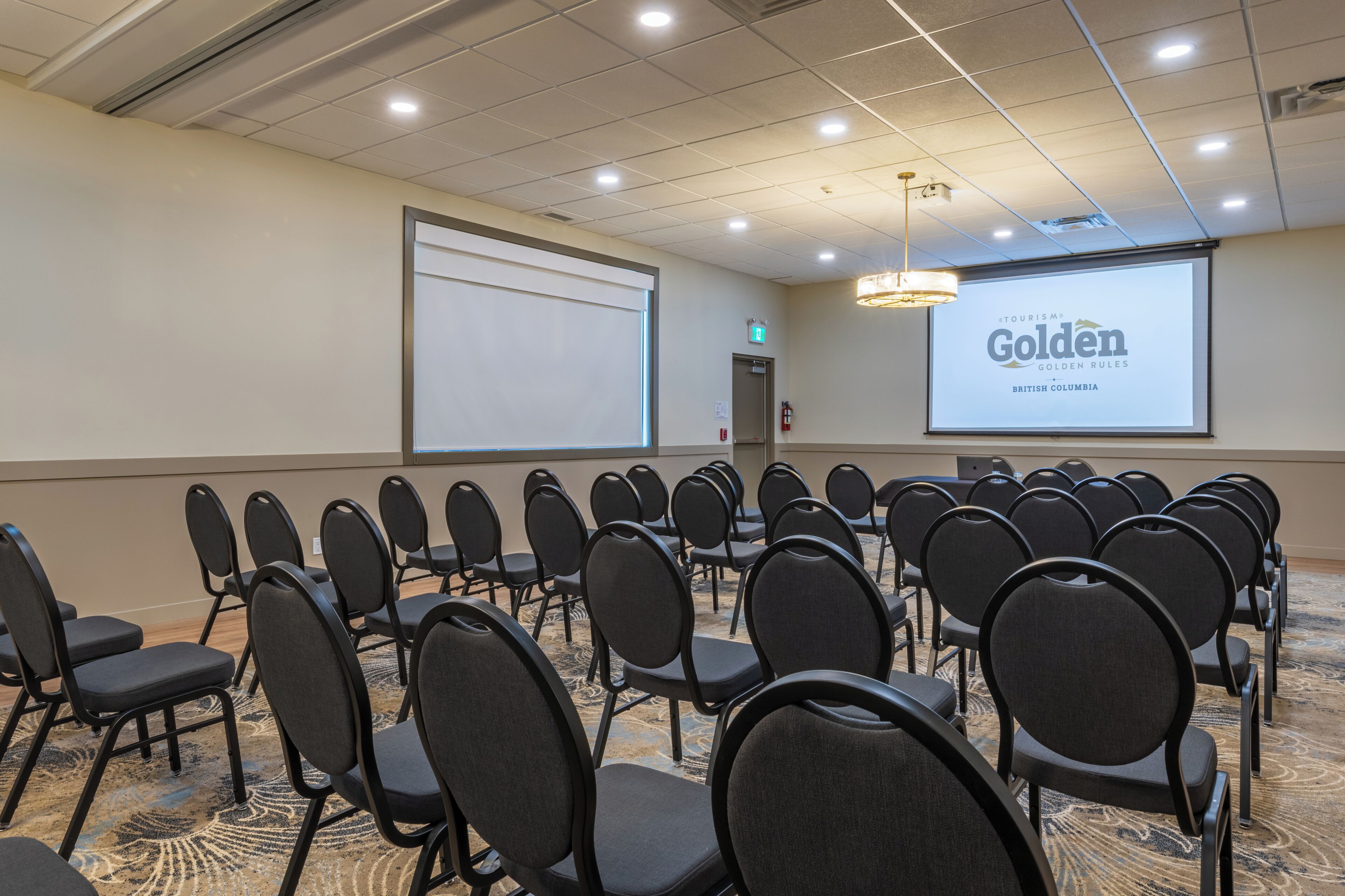 A conference room with rows of chairs, a projector screen, and a carpeted floor.