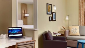 Ein Hotelzimmer mit Schreibtisch, Laptop, Stuhl, Sofa und einem kleinen Tisch mit Lampe.
